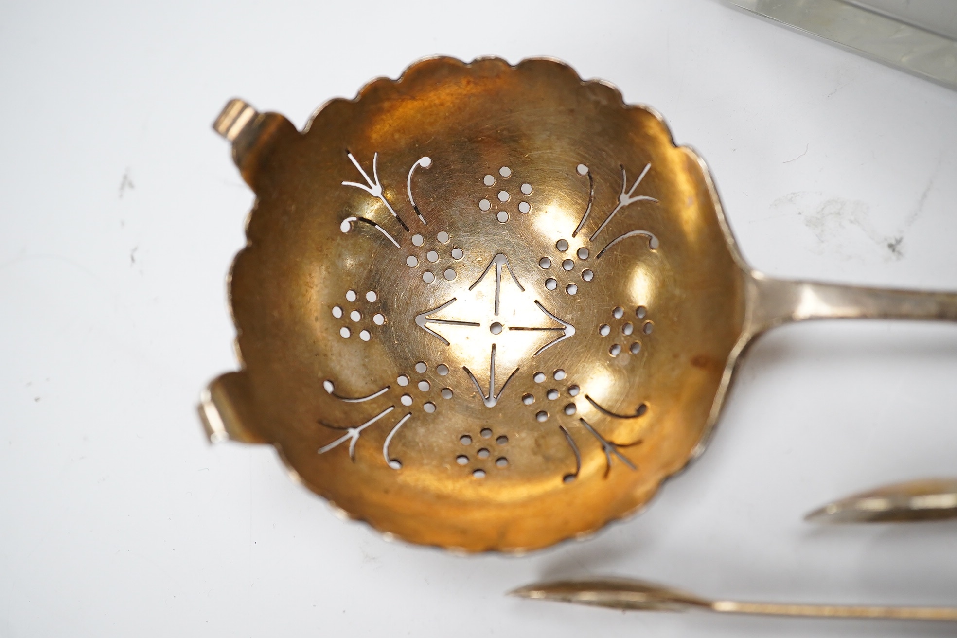 Two square silver topped glass preserve pot, two pairs of George III silver sugar tongs, a silver tea strainer and a caddy spoon. Condition - fair